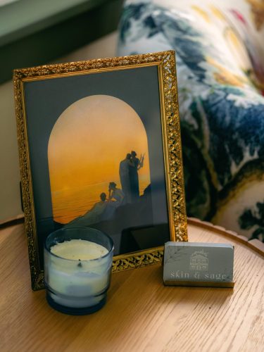 Framed photo of women at sunset sits on a wooden side table with candle and business cards